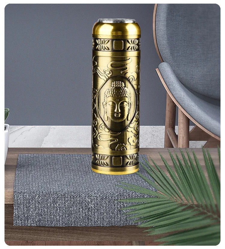 Gold-colored water bottle with Buddha design on a wooden table with a gray chair and plant in the background.